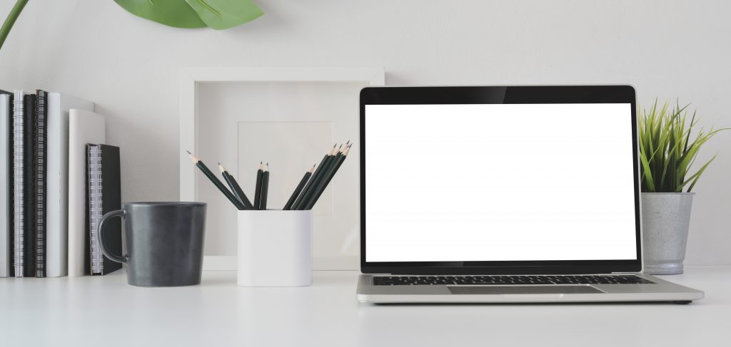 A laptop on a white desk with notebooks, pencils, and a plant